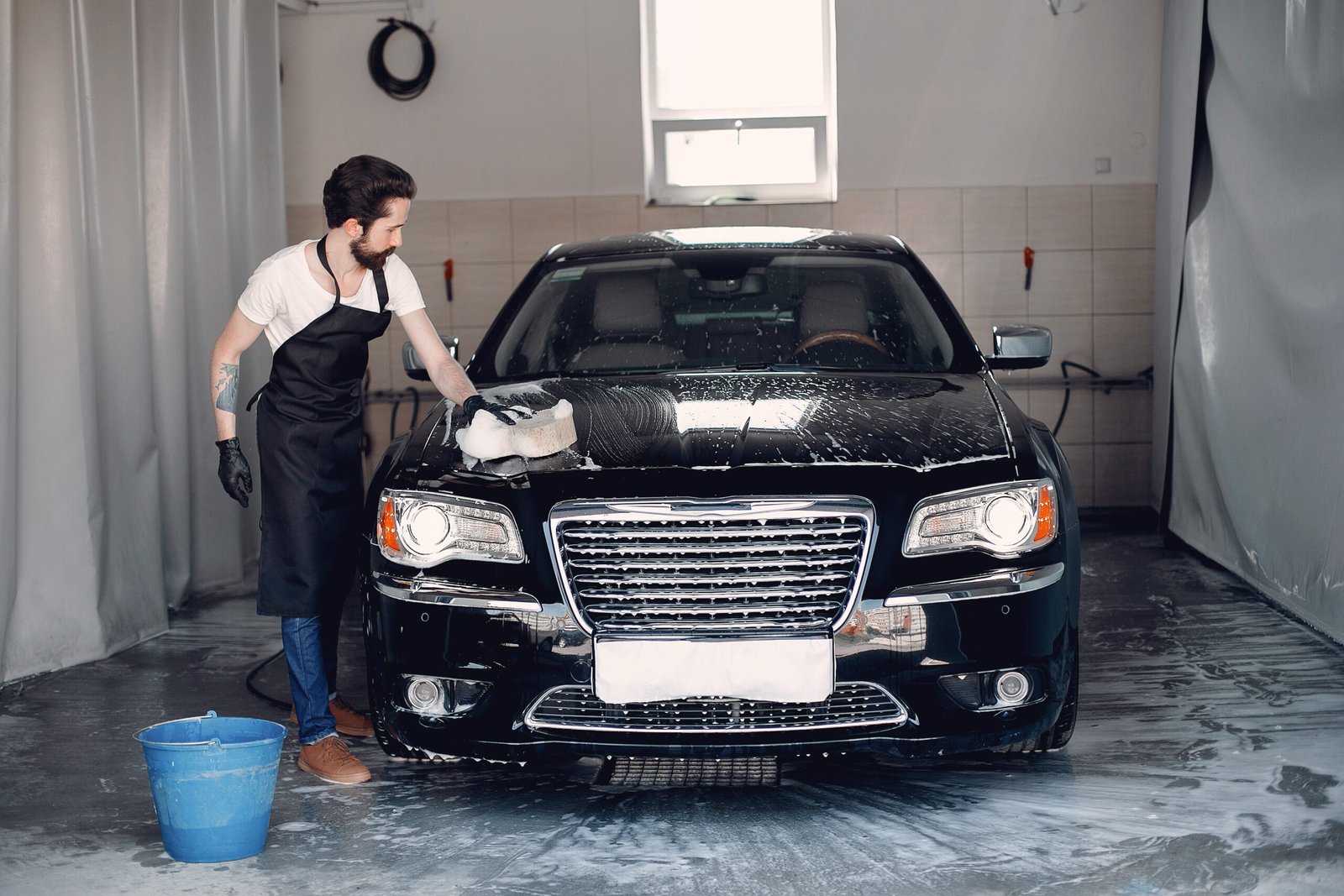 Man in a garage. Worker washing a car. Guy with a bucket ans sponge